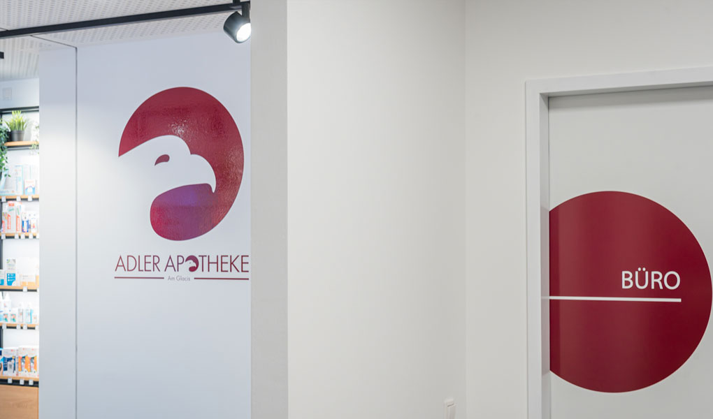 Grafik und Wegleitsystem in einer Apotheke. Man sieht einen weißen Adlerkopf in einem roten Kreis sowie eine Türbeklebung als roter Kreis mit dem weißen Schriftzug Büro.