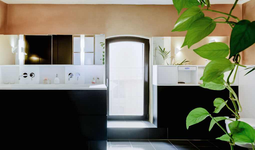 Einbauschränke in einem Bad. Schwarze und weiße Elemente. Im Bild rechts ragt eine Hängepflanze ins Bild.