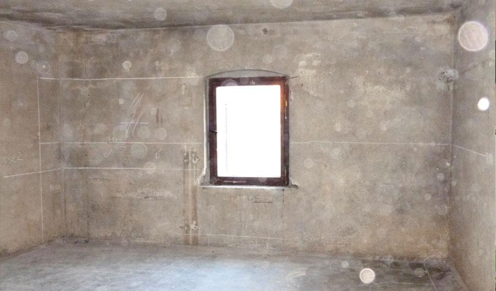 Vorherbild von einer Dachbodenkammer mit graubraunen rohen Wänden und einem kleinen Fenster in der Mitte.