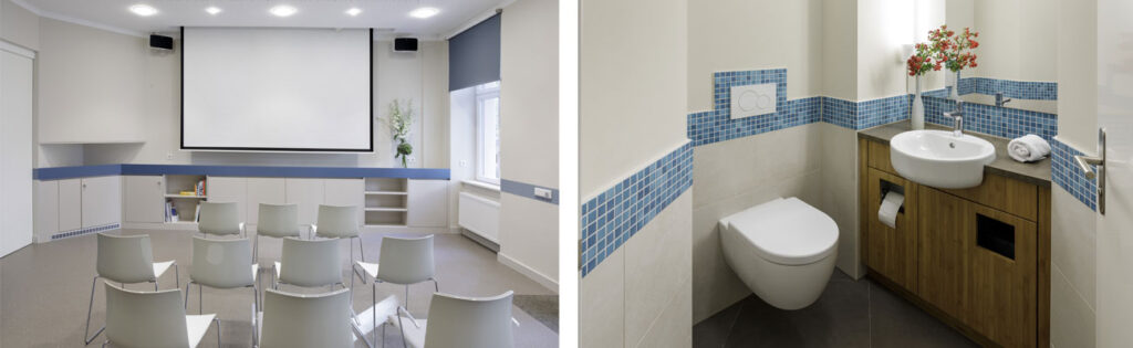 Ein Doppelbild: links sieht man einen Veranstaltungsraum mit weißen Stühlen und einer heruntergezogenen Leinwand. umlaufend auf den grauen Möbeln und grauen Wänden verläuft ein blauer Streifen. Rechts sieht man das WC dazu. Es gibt auch hier einen umlaufenden Streifen mit blauen Mosaikfliesen. Das Waschbecken ist in einen Holzschrank eingebaut.