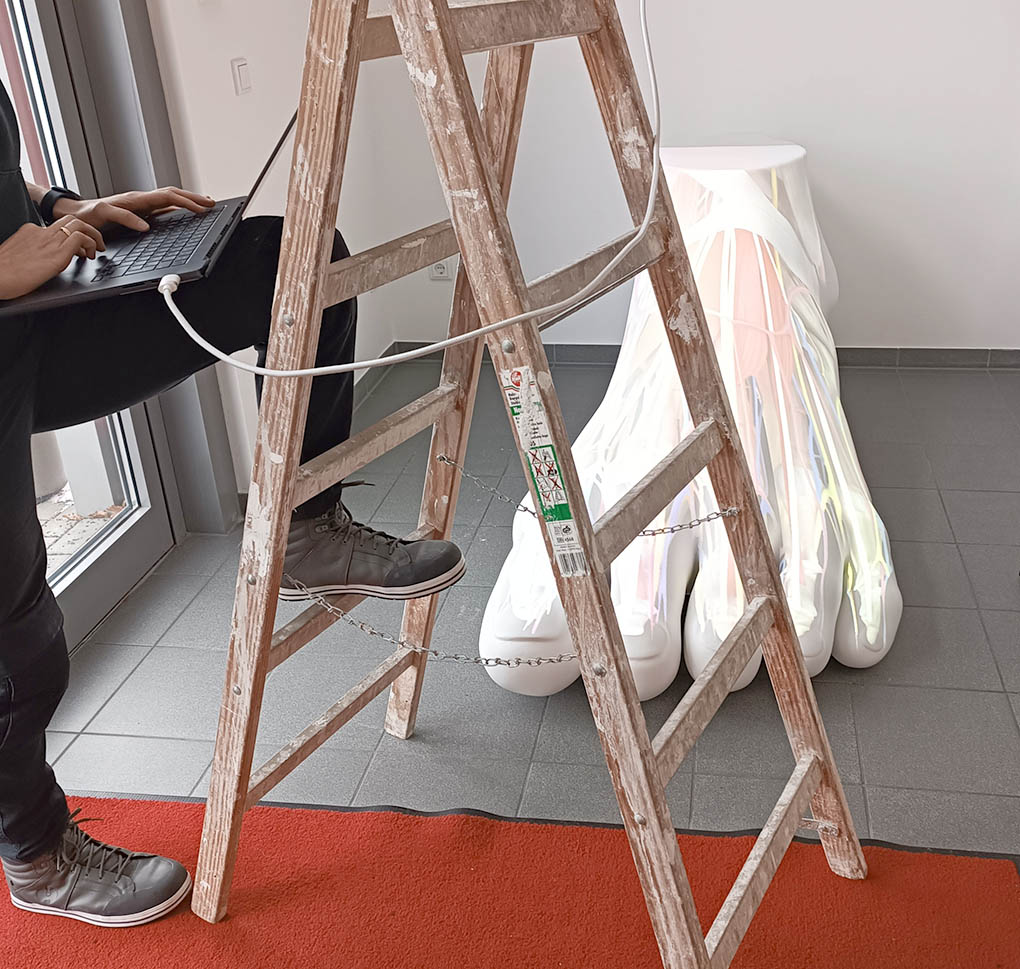 Ein Bild zum Thema Mapping und Konfiguration: Im Hintergrund ein überdimensionaler weißer Fuß mit einer anatomischen Projektion von Muskeln und Blutgefäßen. Davor steht eine Holzleiter. Am linken Bildrand erkennt man angeschnitten eine Person, die einen Fuß auf die Leiter stellt und am Laptop etwas programmiert.