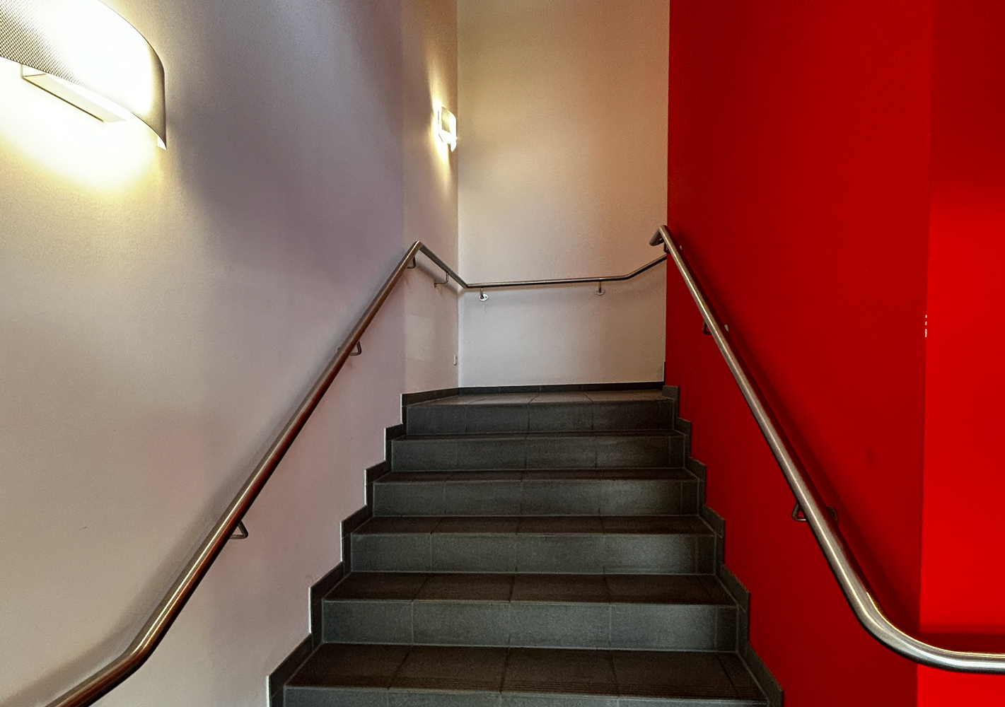 Vorher-Bild eines Treppenaufgangs. Weiße Wände und graue Fliesen. Die rechte Wand ist strahlend rot.