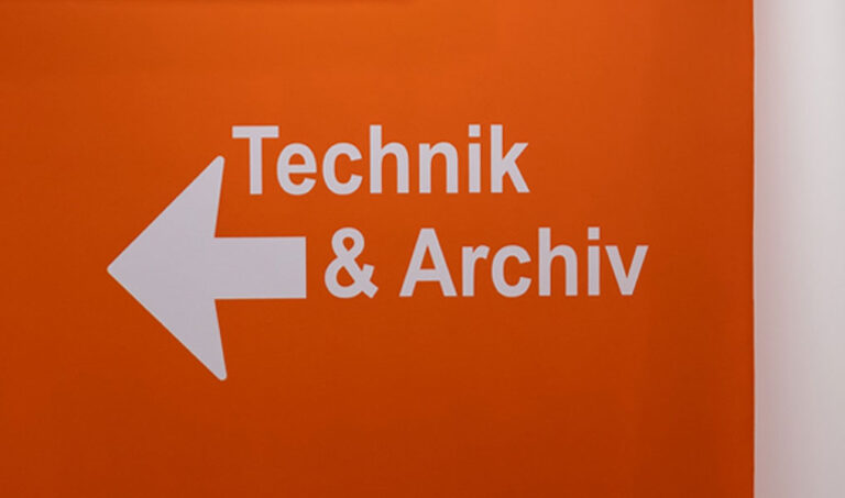 Orange Wand mit der Aufschrift Technik und Archiv und einem Pfeil. Es ist das Themenbild zu einem Beitrag zu Orientierung und Wegeleitung und der Begriffsbestimmung in diesem Themenfeld.
