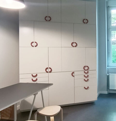 Küchenschrank aus weißen Möbeln, asymmetrisch angeordnet, mit roten Griffen.