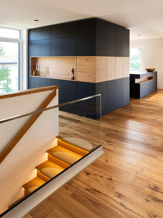 moderne schwarze Einbauschränke und beleuchtete Treppe, Eicheparkett in großzügigem Wohngeschoss einer Villa.