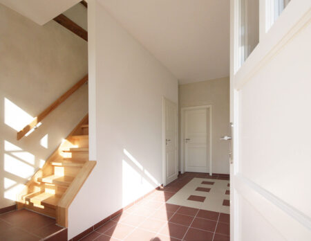 Blick in einen Wohnbereich mit Buchetreppe, weißen Wänden und rot-weißem Fliesenboden.