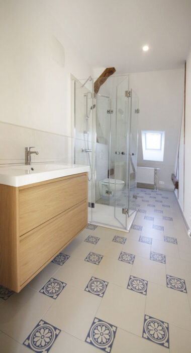 Neues Bad in einem denkmalgeschützten Haus. Dusche mit Klapp-Glastür. Im Vordergrund ein Waschtisch mit Eiche-Unterschrank.